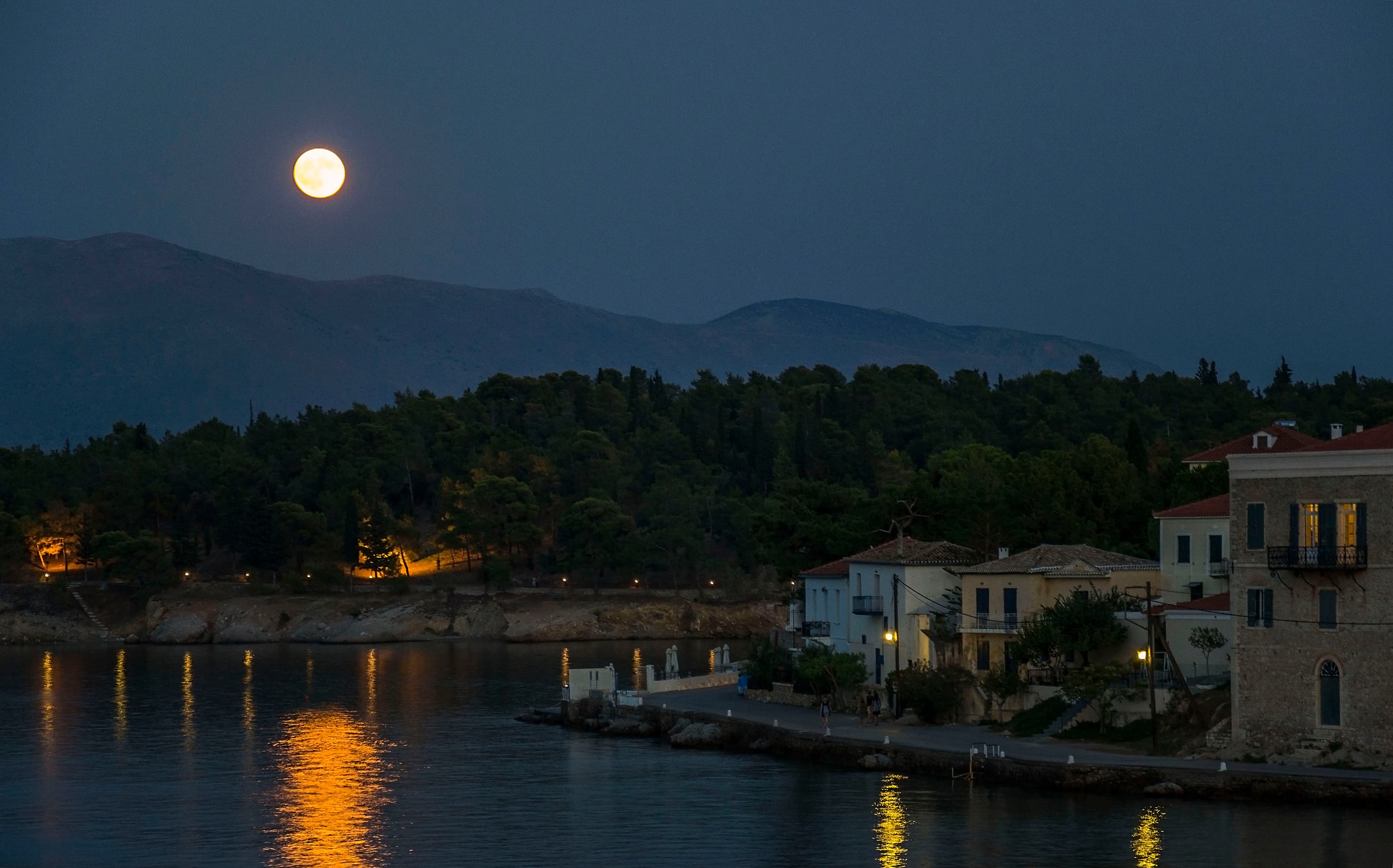A moonlit waterfront with warm reflections on the water.
