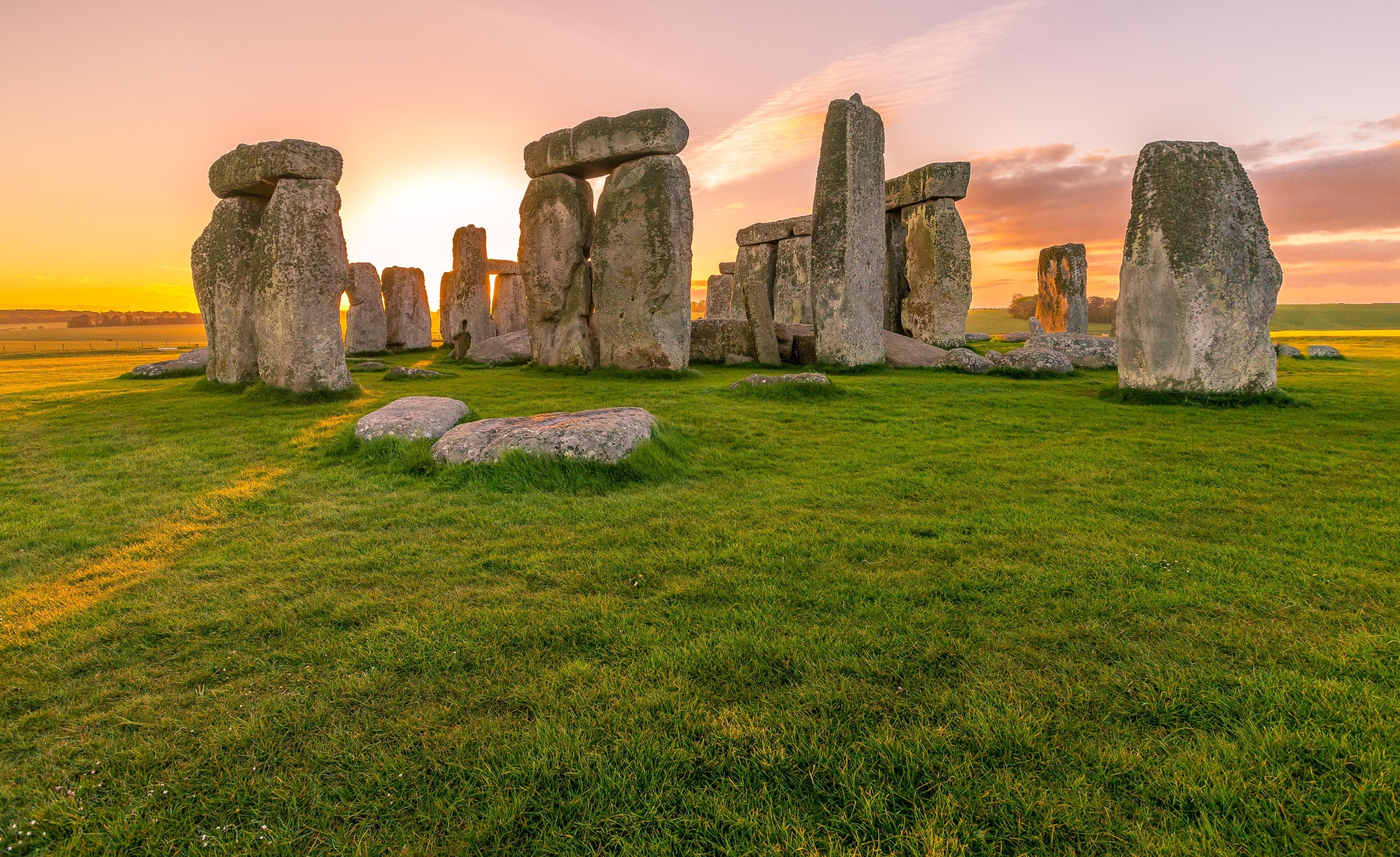 Stonehenge at sunset over green grass.